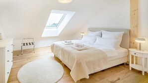 Un dormitorio con cama, mesitas de noche, una ventana pequeña y un tragaluz.