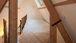 Et soveværelse med skrå vægge, loft, træbjælker, seng og et vindue.