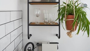 Et køkken med en sort metalkapel, en hængende plante, en elkedel og en hvid maskine på bordet.