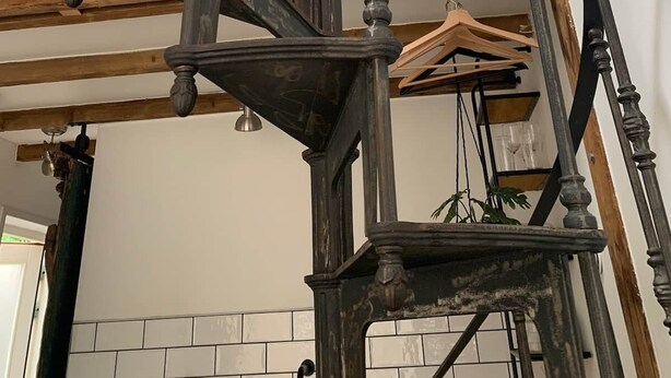 En spiralformet trappe med træloft og en vægmonteret lampe.