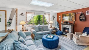 Ein gemütliches Wohnzimmer mit Kamin, karierten Sofas, einem blauen Hocker und einem Schild mit der Aufschrift Ski Lift an der Wand.