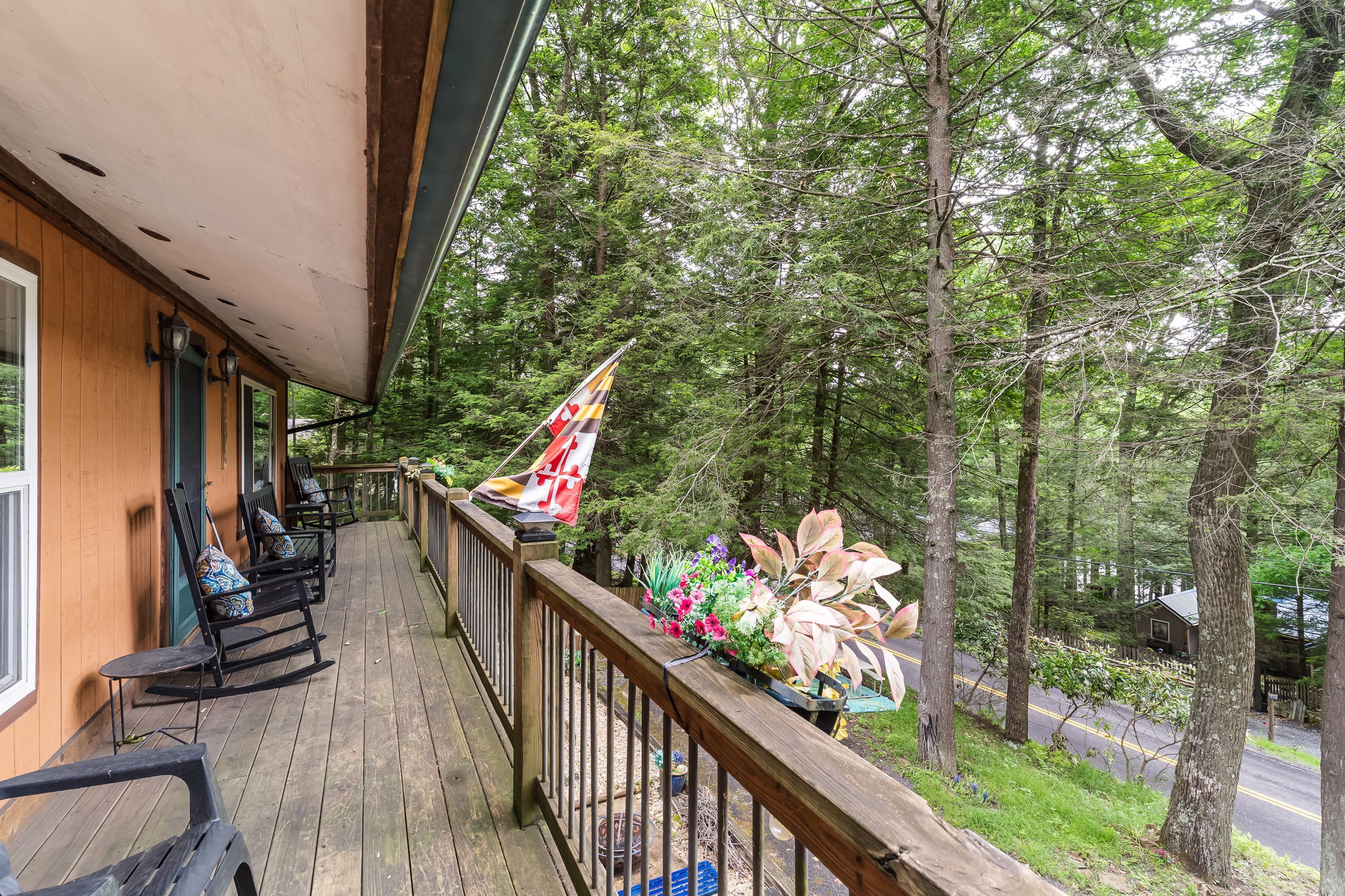 A wooden deck with rocking chairs, a flag, and a view of a forest.