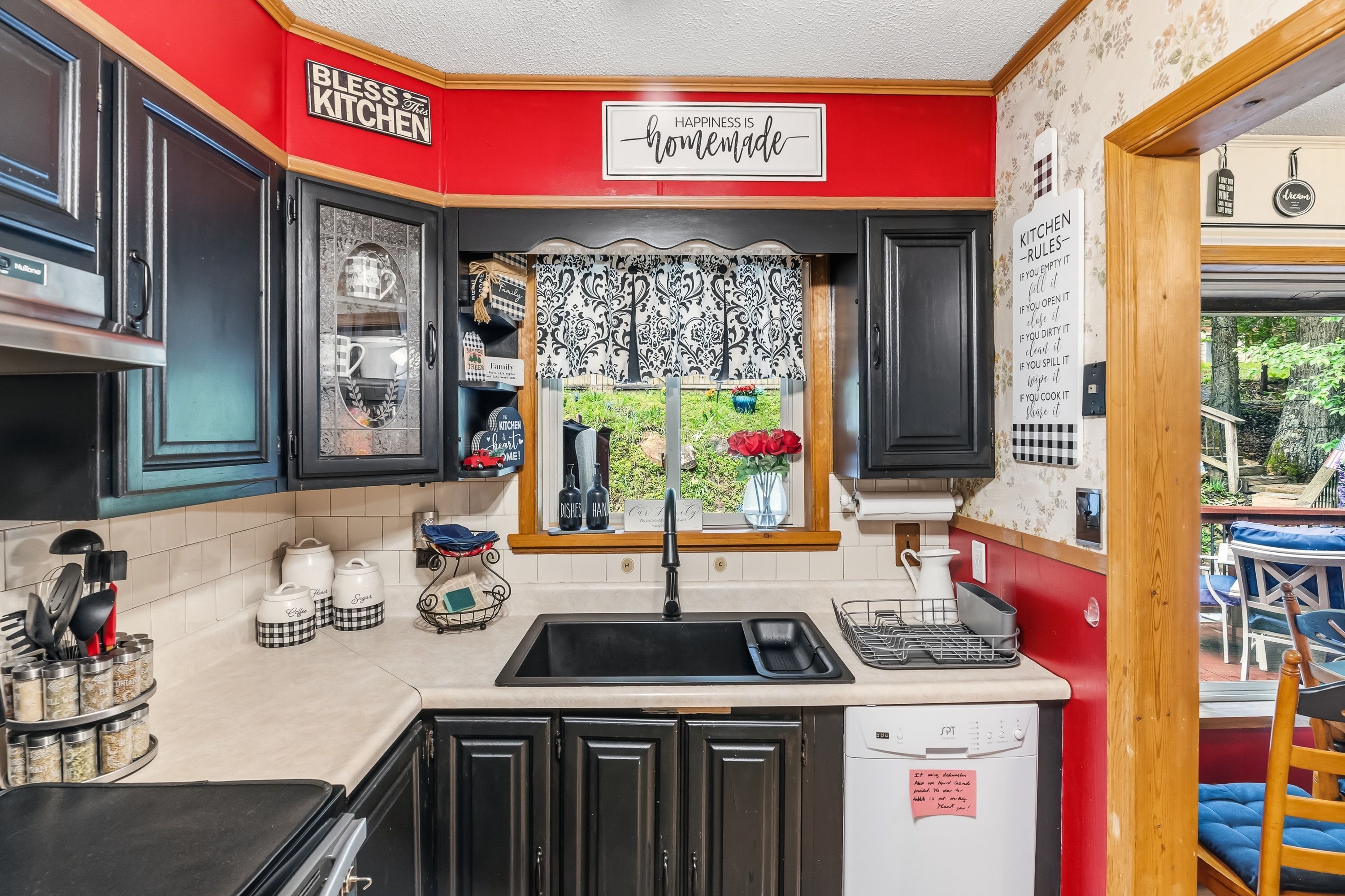 A kitchen with black cabinets, a red accent wall, and a window with patterned curtains.
