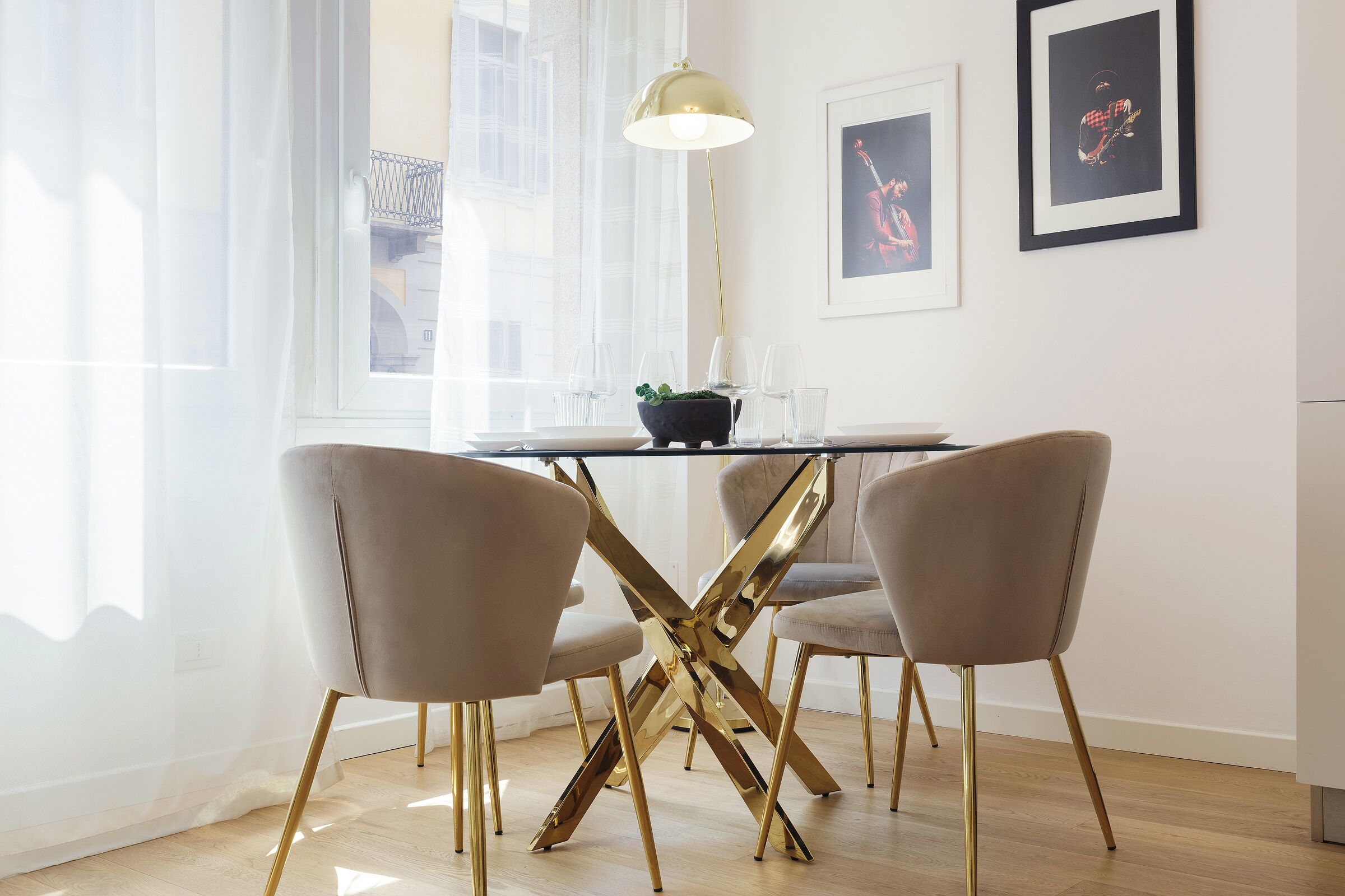 Un coin repas avec une table en verre, deux chaises, une suspension et des œuvres d’art encadrées accrochées au mur.