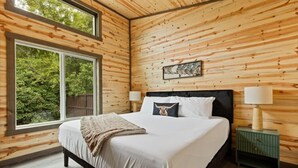 Un dormitorio con una cama grande, paredes de madera, una ventana y una mesita de noche.