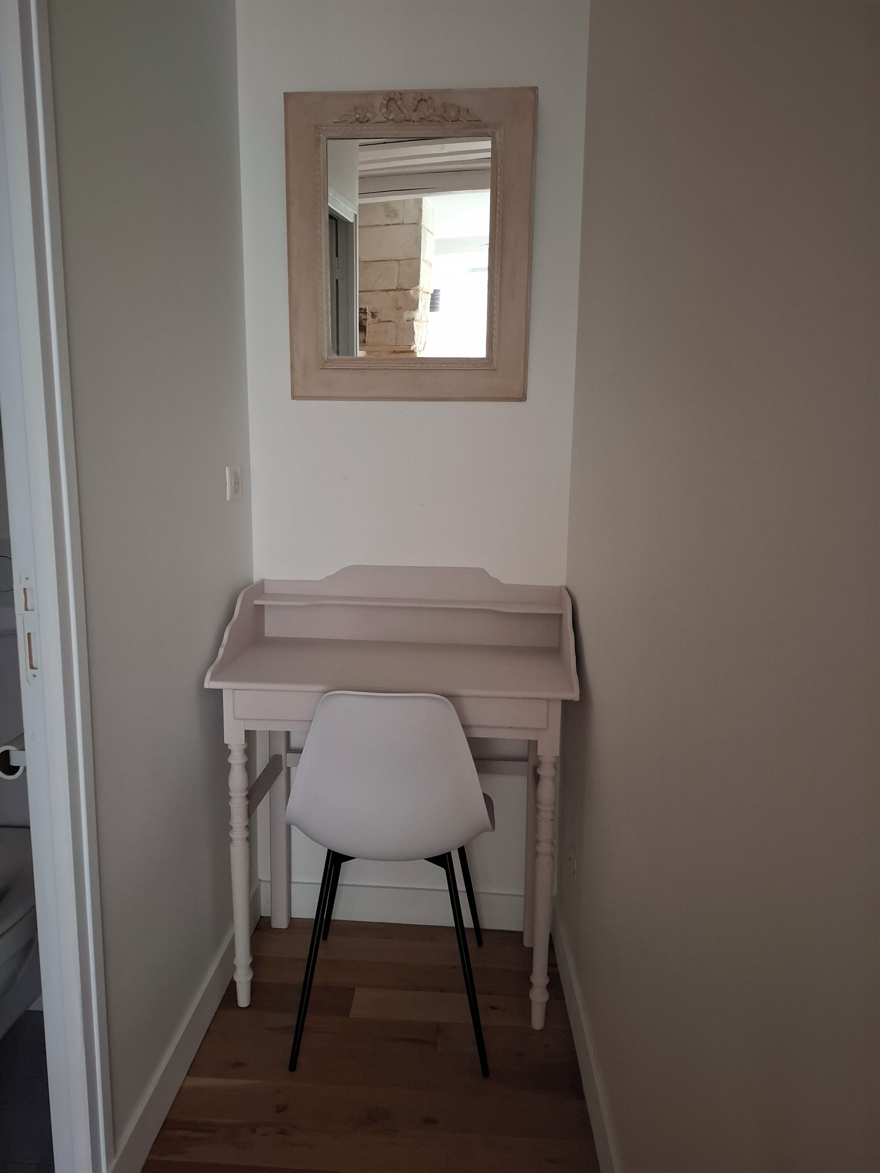 A room with a white desk, a white chair, and a mirror on the wall.