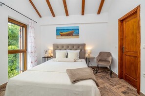 A bedroom with a bed, a chair, a painting, and a wooden door. - Villa OASA with private heated pool (Ljutići)