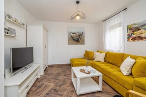 A living room with a television, a yellow sofa, a white coffee table, and a painting on the wall. - Villa OASA with private heated pool (Ljutići)