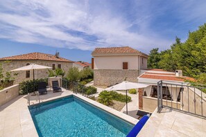 A swimming pool with a stone wall, a lounge chair, and a small building with a tiled roof. - Villa OASA with private heated pool (Ljutići)