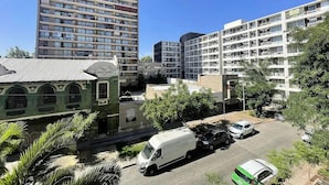 A multi-story residential building with balconies, a parking area, and a green building with arched windows. - Rbk Dpto new a pasos del Movistar Arena (Santiago)