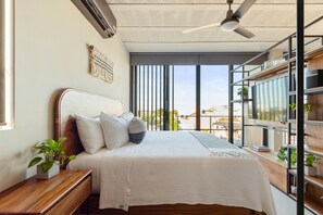 A modern bedroom with a bed, bedside table, and a view through large windows. - Ocean Boutique Condos (Playa del Carmen)