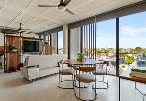 A modern living room with a sofa, dining table, chairs, a TV, and large windows offering a city view. - Ocean Boutique Condos (Playa del Carmen)