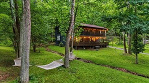 Eine Hütte mit einer Terrasse und Lichterketten, umgeben von Bäumen und Gras.