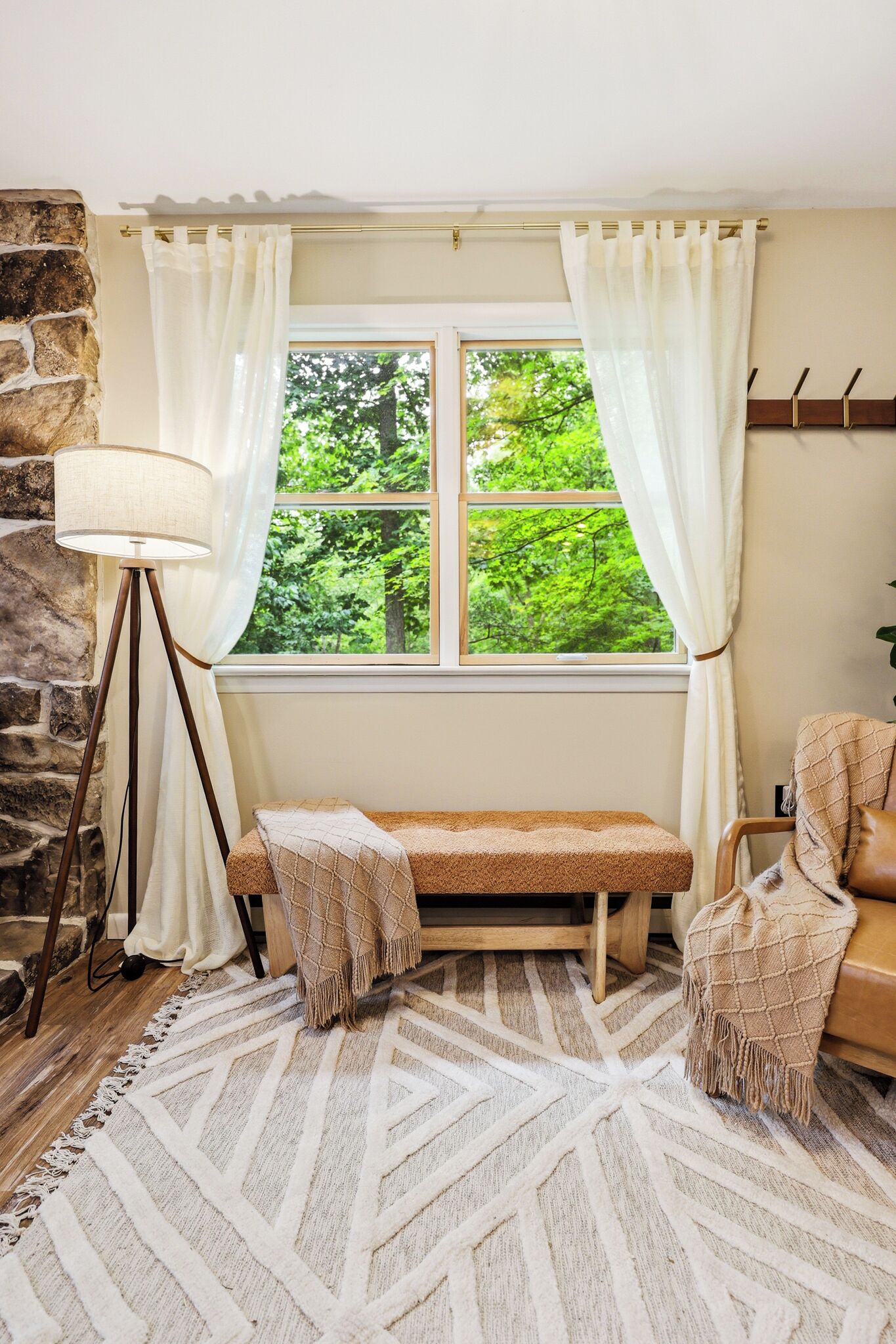 Una habitación con pared de piedra, un banco, una lámpara de pie y una ventana con cortinas.