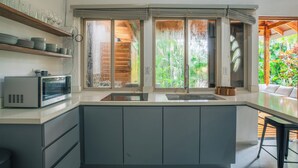 A modern kitchen with a built-in microwave, a sink, and a wooden shelf with dishes. - Tranquil Jungle Nest Near Guiones Surf with Pool (Guanacaste Province)