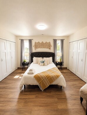 A bedroom with a large bed, two nightstands, a ceiling light, and a view of the outdoors.