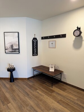 Ein Zimmer mit Holzboden, einem schwarzen Tisch mit weißer Willkommensauslage, einer Wanduhr, einem gerahmten Willkommensschild und einem gerahmten abstrakten Gemälde.