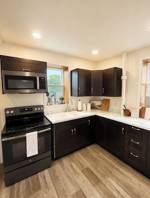A modern kitchen with dark cabinets, a stainless steel stove, and a microwave.