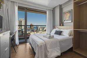 A hotel room with a bed, a desk, a chair, a TV, a large window with curtains, and a painting on the wall. - Atlantic Ocean Barra Near the Lighthouse, Porto Beach and Barra Shopping by Carpediem (Salvador)