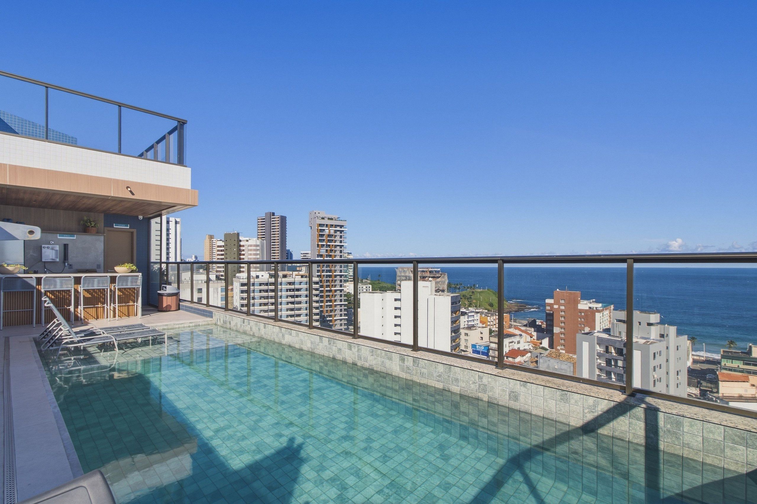 A rooftop pool with a city view, a balcony with a railing, and a small seating area with chairs and a table.