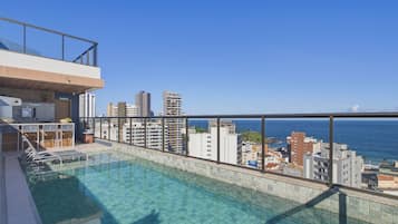 A rooftop pool with a city view, a balcony with a railing, and a small seating area with chairs and a table.