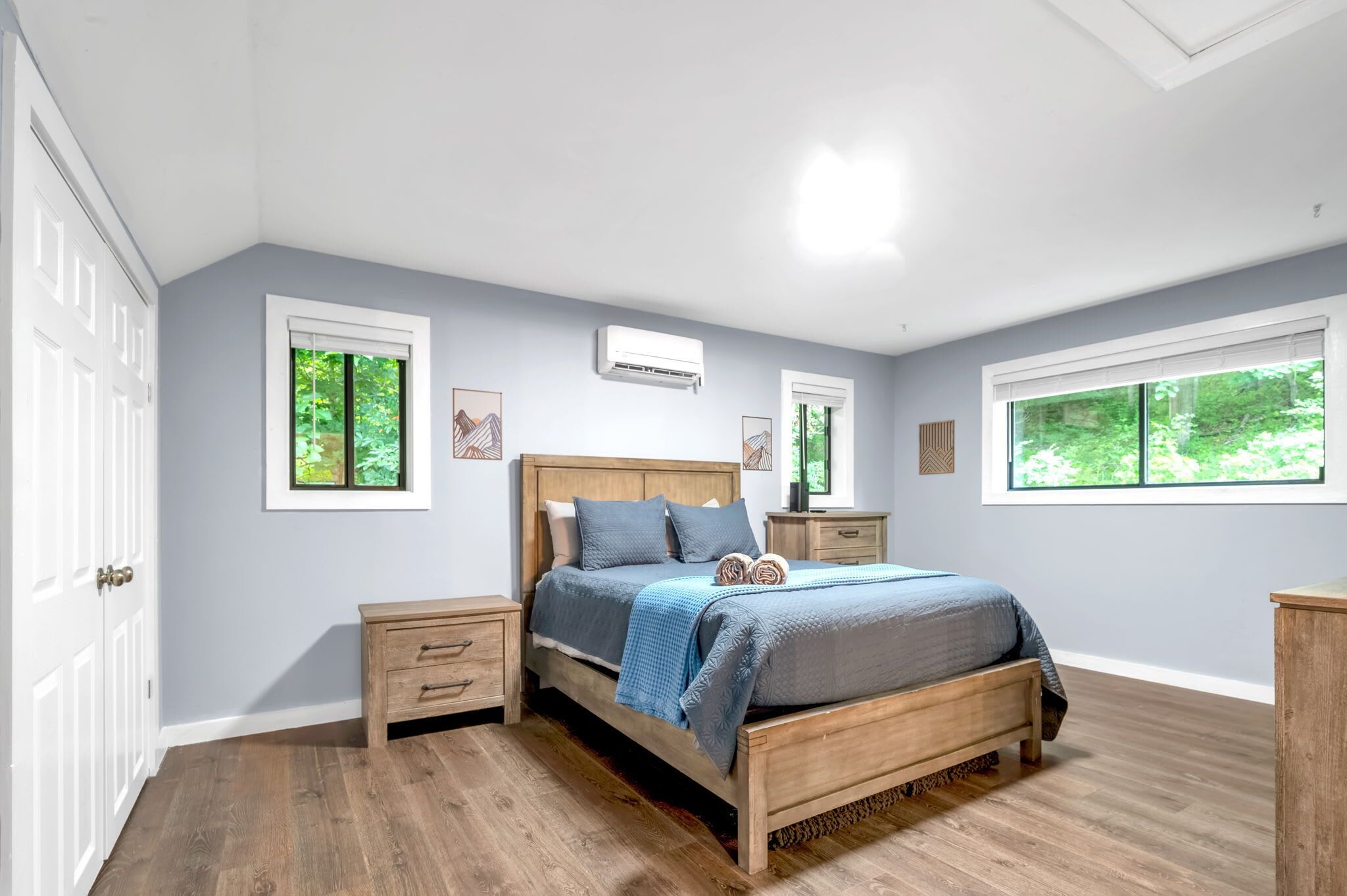 Une chambre à coucher avec un lit en bois, deux tables de chevet, une commode et une fenêtre donnant sur un paysage verdoyant.