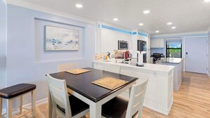 Una cocina moderna con armarios blancos, una isla central y un comedor con una mesa oscura y sillas blancas.