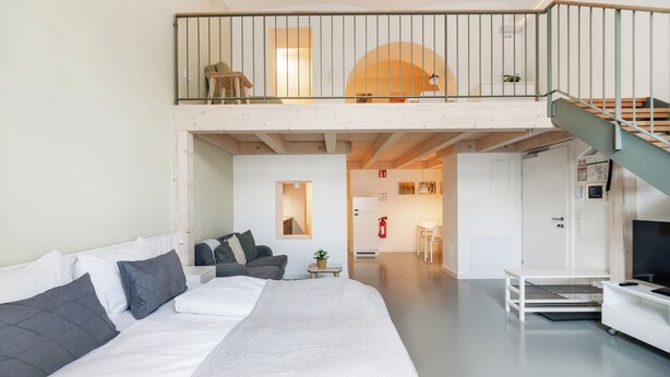 A modern hotel room with a large bed, a sofa, a balcony, and a staircase. - Vorgarten Apartments—central, new, and stylish for a comfortable stay in Vienna (Wien)