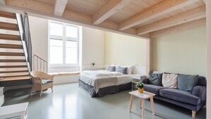 A modern bedroom with a bed, a sofa, a chair, a small table, and a staircase. - Vorgarten Apartments—central, new, and stylish for a comfortable stay in Vienna (Wien)
