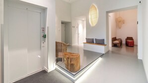 A modern hotel lobby with a glass partition, a wooden tree stump, wicker chairs, and a wall-mounted light fixture. - Vorgarten Apartments—central, new, and stylish for a comfortable stay in Vienna (Wien)
