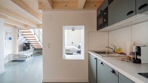 A modern kitchen with grey cabinets, a built-in microwave, and a window overlooking a bedroom. - Vorgarten Apartments—central, new, and stylish for a comfortable stay in Vienna (Wien)