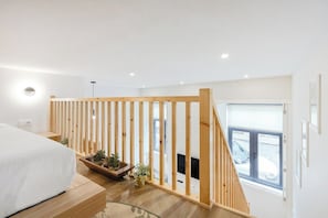 Ein Schlafzimmer mit einem Bett, einem Holllaufgeländer, einem Fenster und einem Kamin.