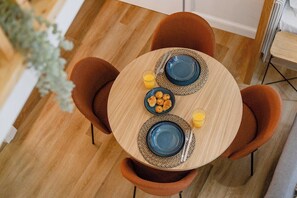 Ein runder Holztisch mit blauen Tellern, orangefarbenen Stühlen und einem kleinen Glas Saft.