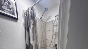 Ein kleiner, abgeschlossener Duschbereich mit Duschkopf, einer Glasdusche und einem gefliesten Boden.