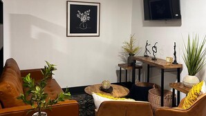Ein modernes Wohnzimmer mit einer Couch, Sesseln, einem Couchtisch und einem an der Wand montierten Fernseher.