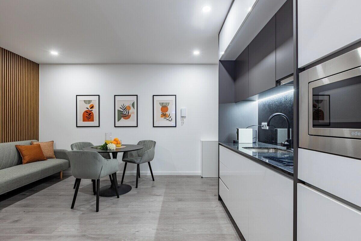Une cuisine moderne dotée d’un four encastré, un coin repas avec une table ronde et des chaises, et trois œuvres d’art encadrées accrochées au mur.