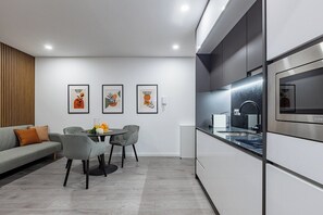 A modern kitchen with a built-in oven, a dining area with a round table and chairs, and three framed artworks on the wall. - Doce como Laranja @ Boavista Executive Studios (Porto)