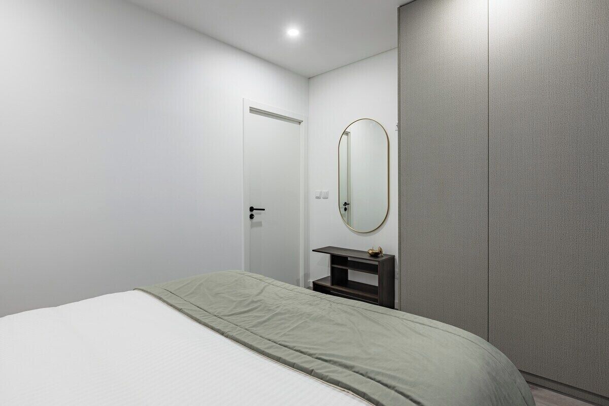 A bedroom with a bed, a door, a mirror, and a wardrobe.