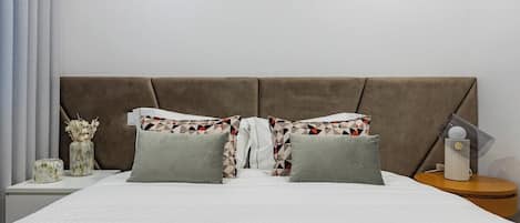 A bed with a headboard, pillows, a bedside table, and a vase with dried flowers.