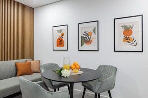 A modern living room with a grey sofa, a round dining table with chairs, and three framed abstract artworks on the wall. - Doce como Laranja @ Boavista Executive Studios (Porto)