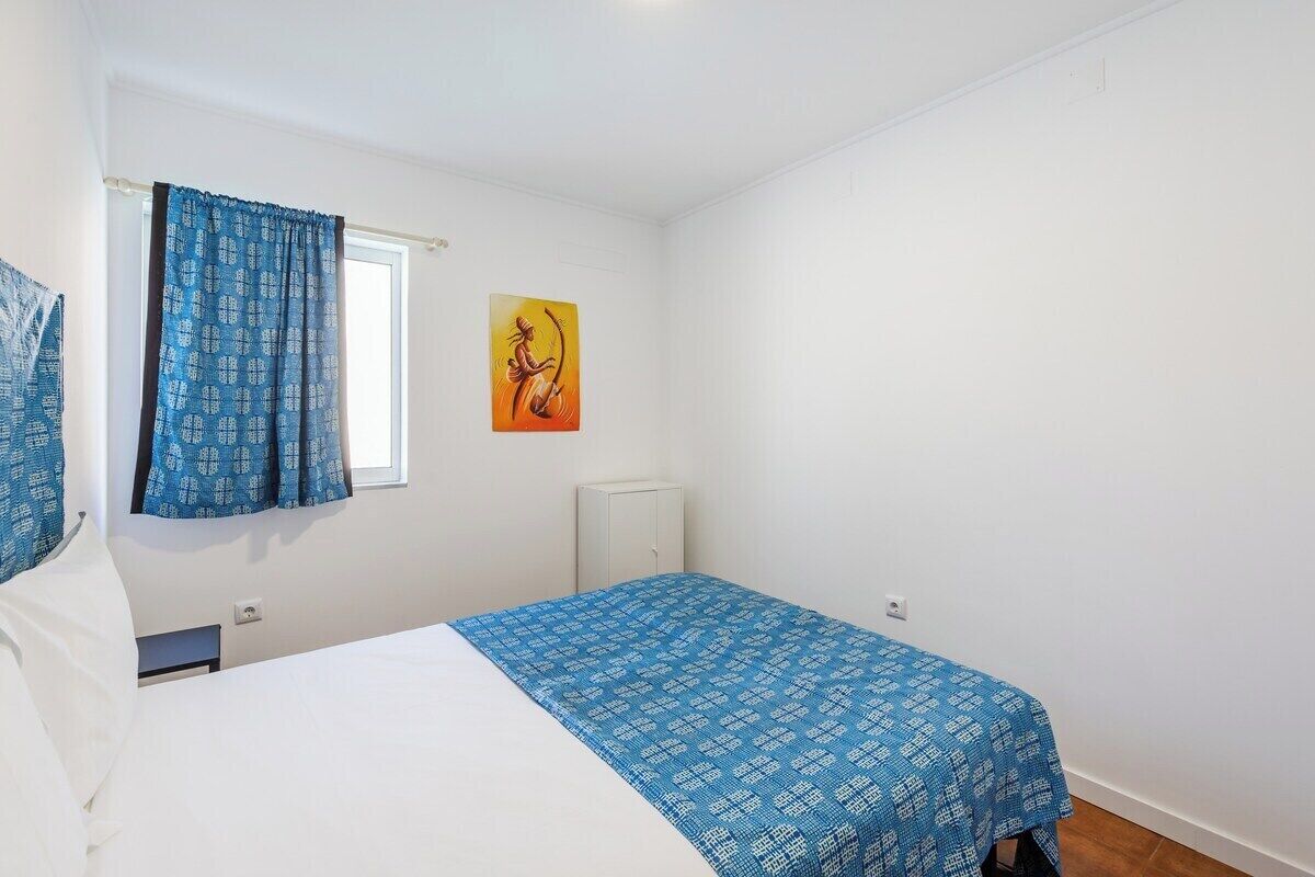A bedroom with a bed, a window with curtains, a radiator, and a wall-mounted artwork.