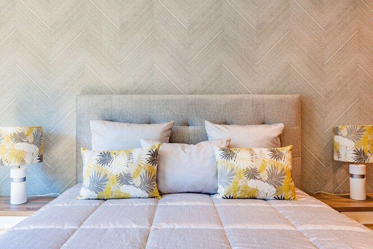 Un lit avec une tête de lit matelassée, deux tables de chevet avec des lampes et un mur orné d’un motif.