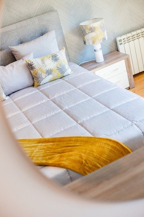 A bed with a quilted cover, a bedside table with a lamp, and a radiator. - Gaia Elegant Retreat II (Canidelo)