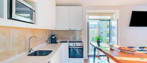 A compact kitchen with a microwave, oven, sink, and a dining area with stools.