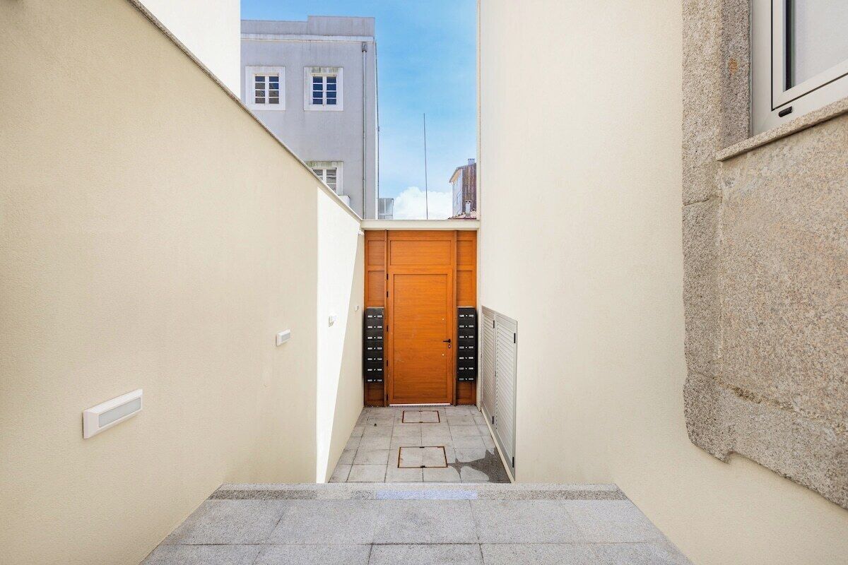 Un pasillo estrecho con una puerta de madera, un radiador y una ventana en la pared derecha.