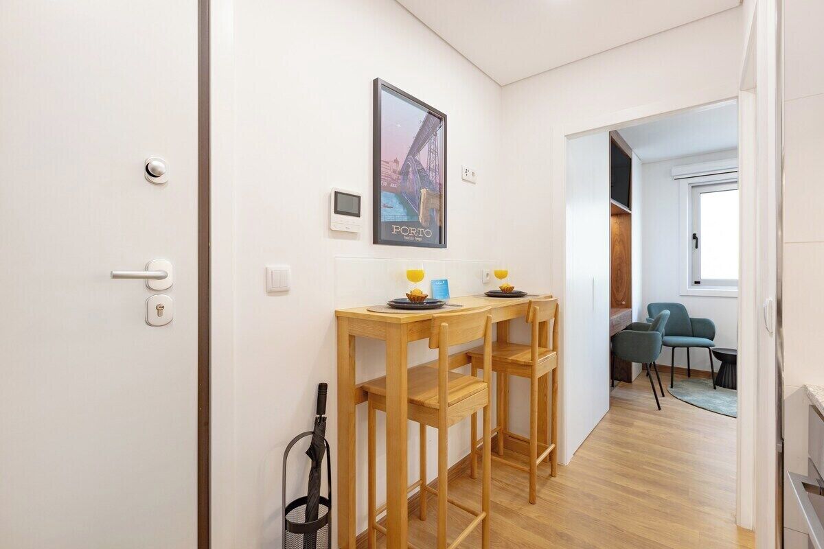 Un pasillo con una mesa y sillas de madera, un cartel en la pared y una puerta con manija.