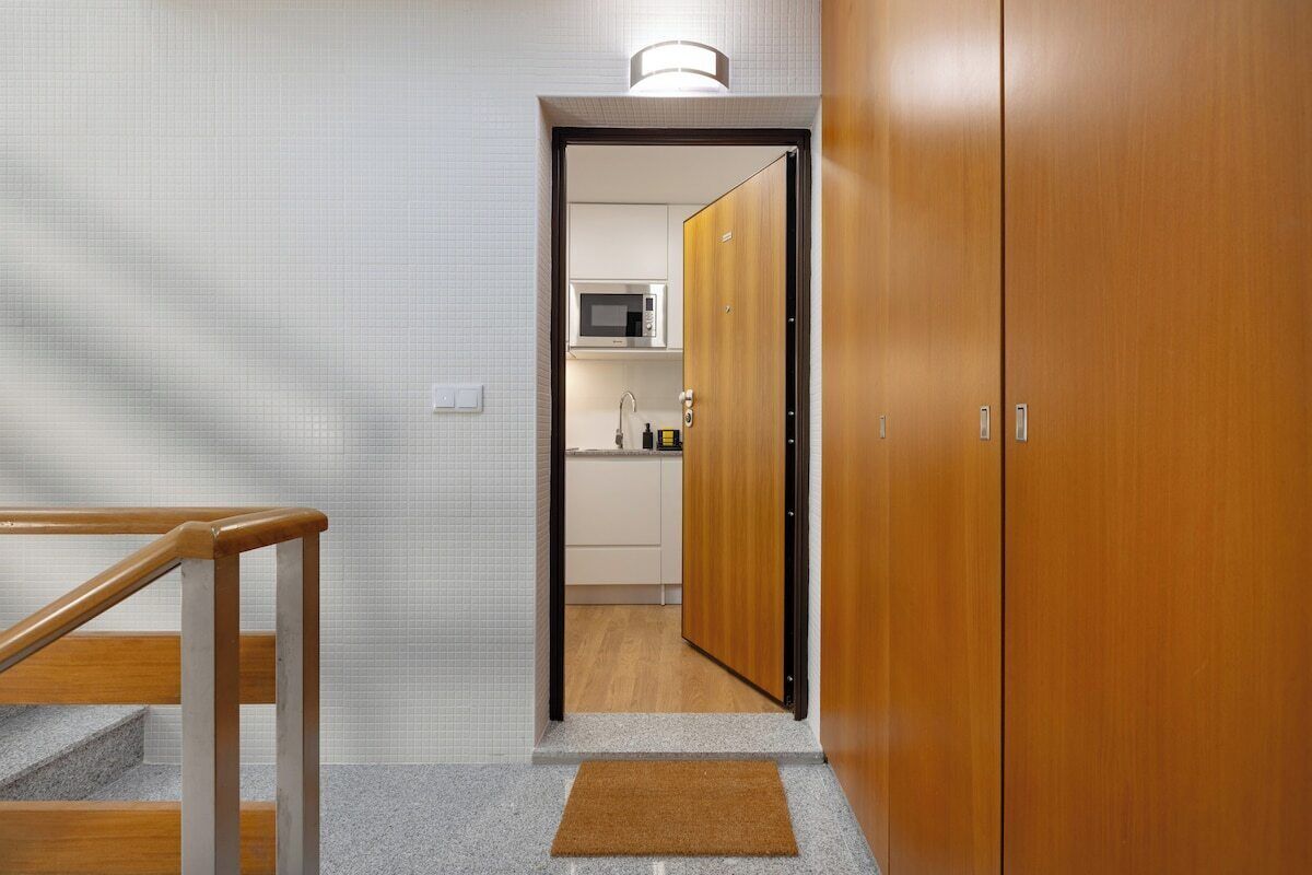 Un pasillo con una puerta de madera que da a una zona de cocina con microondas.