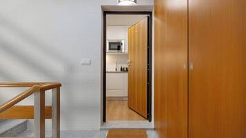 Un pasillo con una puerta de madera que da a una zona de cocina con microondas.