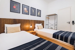 A hotel room with two beds, a wooden headboard, a bedside table with a lamp, and framed floral artwork on the wall. - Twin Room @ Guest Inn 1 Boutique House (campo pequeno)