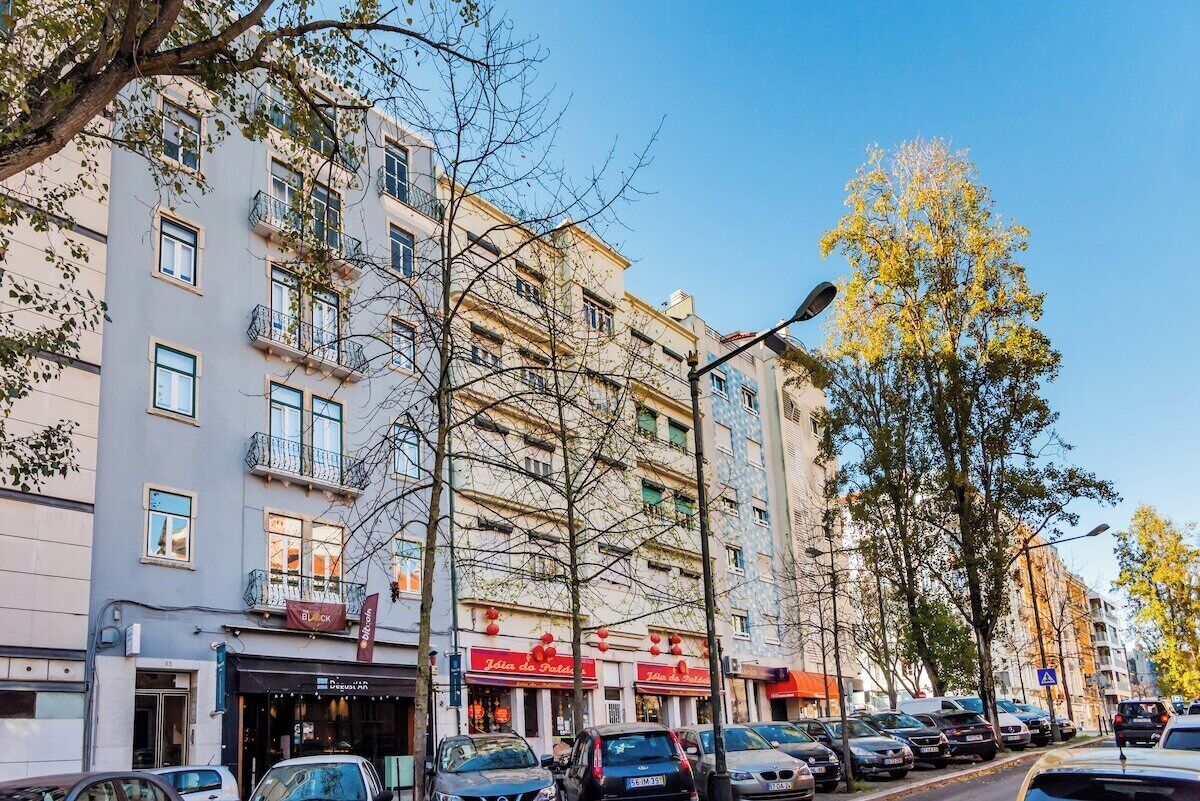 Un immeuble à plusieurs étages, doté de balcons, de devantures de magasins et de voitures garées.